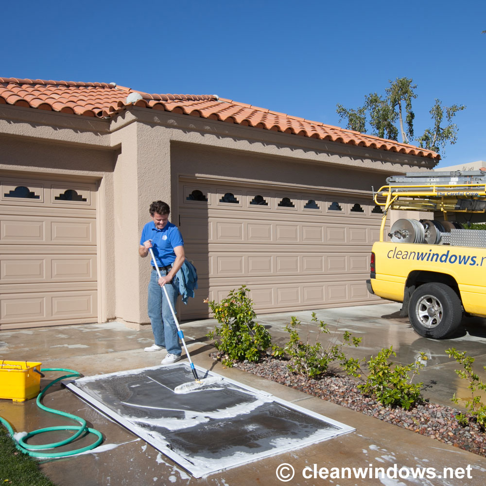 Tim Bloom scrubs a sudsy window screen on a clean driveway outside a home. 