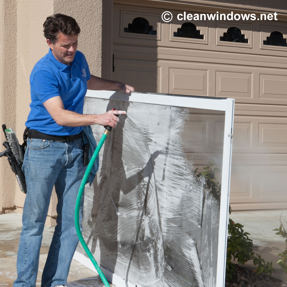Tim Bloom rinses a window screen clean outside a home.