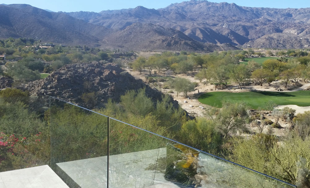 View of a desert golf course from a balcony with clean glass railings. 